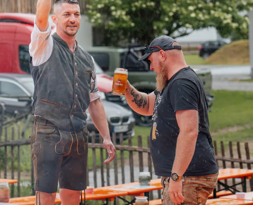 Wir haben uns die Stimmung nicht verderben lassen Zwei Männer mit Maßkrügen stoßen im Regen zwischen nassen Festbänken auf Zoiglbier an.