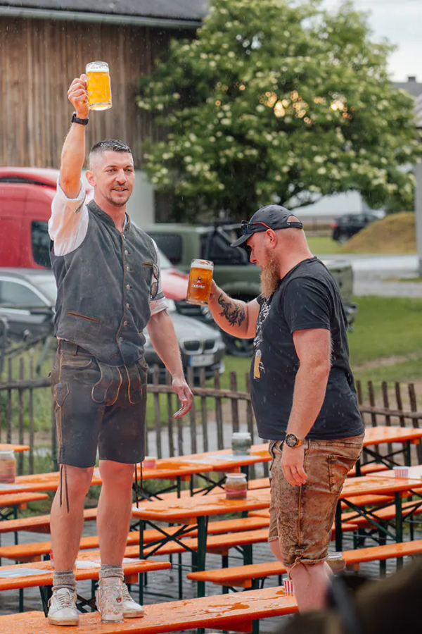 Wir haben uns die Stimmung nicht verderben lassen Zwei Männer mit Maßkrügen stoßen im Regen zwischen nassen Festbänken auf Zoiglbier an.