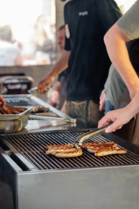 Grillmeister legt Bratwürste mit Zange auf den heißen Rost beim Zoiglbierfest.