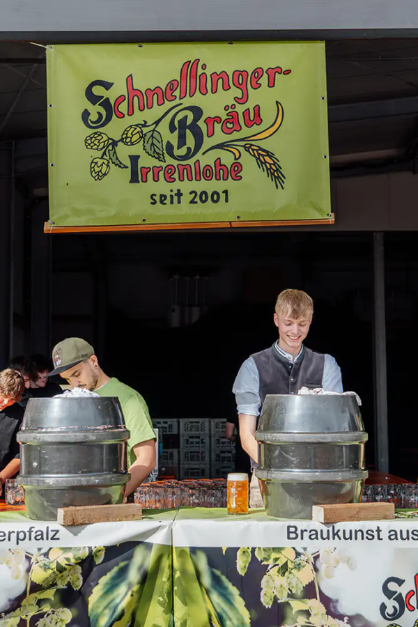 Die Bier-Theke Zapftheke von Schnelllinger-Bräu mit mehreren Fässern und Helfern unter grünem Brauereischild.
