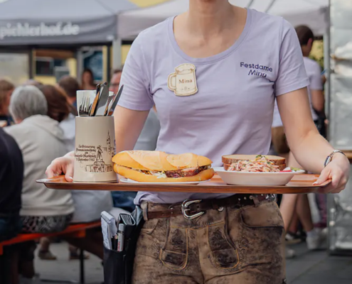Mina beim servieren Bedienung im Festshirt und Lederhosen serviert Brotzeit und Salat auf einem Tablett.