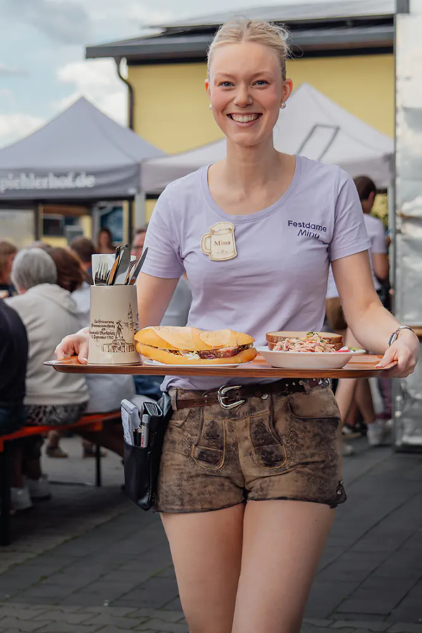 Mina beim servieren Bedienung im Festshirt und Lederhosen serviert Brotzeit und Salat auf einem Tablett.