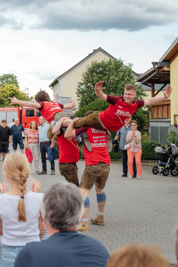 Neidaffer Plattclub Plattlergruppe in roten Shirts wirbeln zwei Tänzer waagerecht durch die Luft vor Publikum.