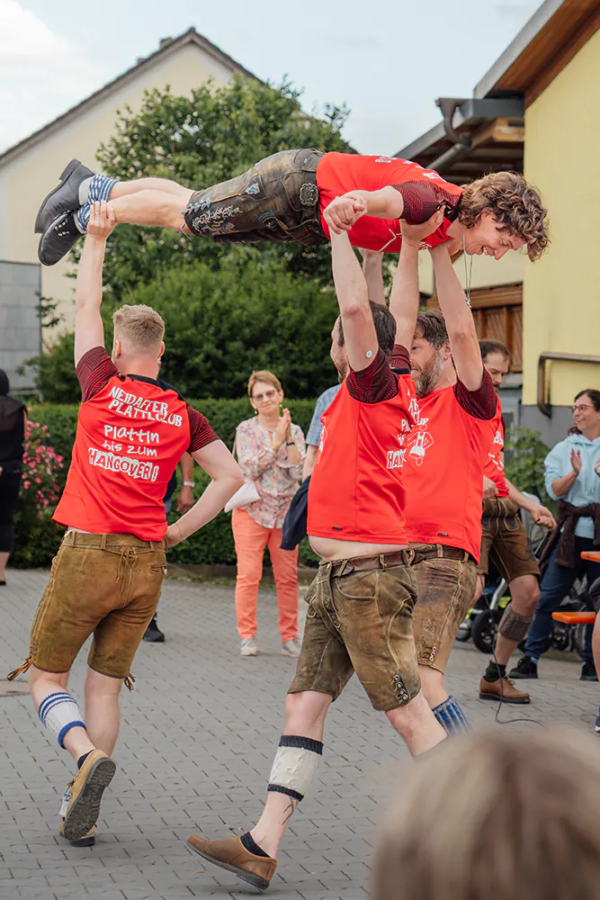 Neidaffer Plattlclub Plattlergruppe trägt einen Tänzer waagerecht durch die Luft über den Festplatz.