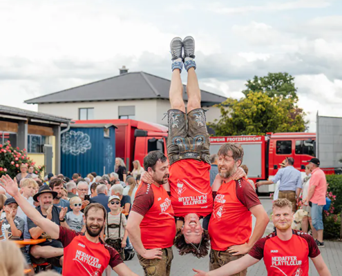 Neidaffer Plattclub Plattlergruppe hebt einen Tänzer kopfüber vor jubelndem Publikum auf dem Hof empor.